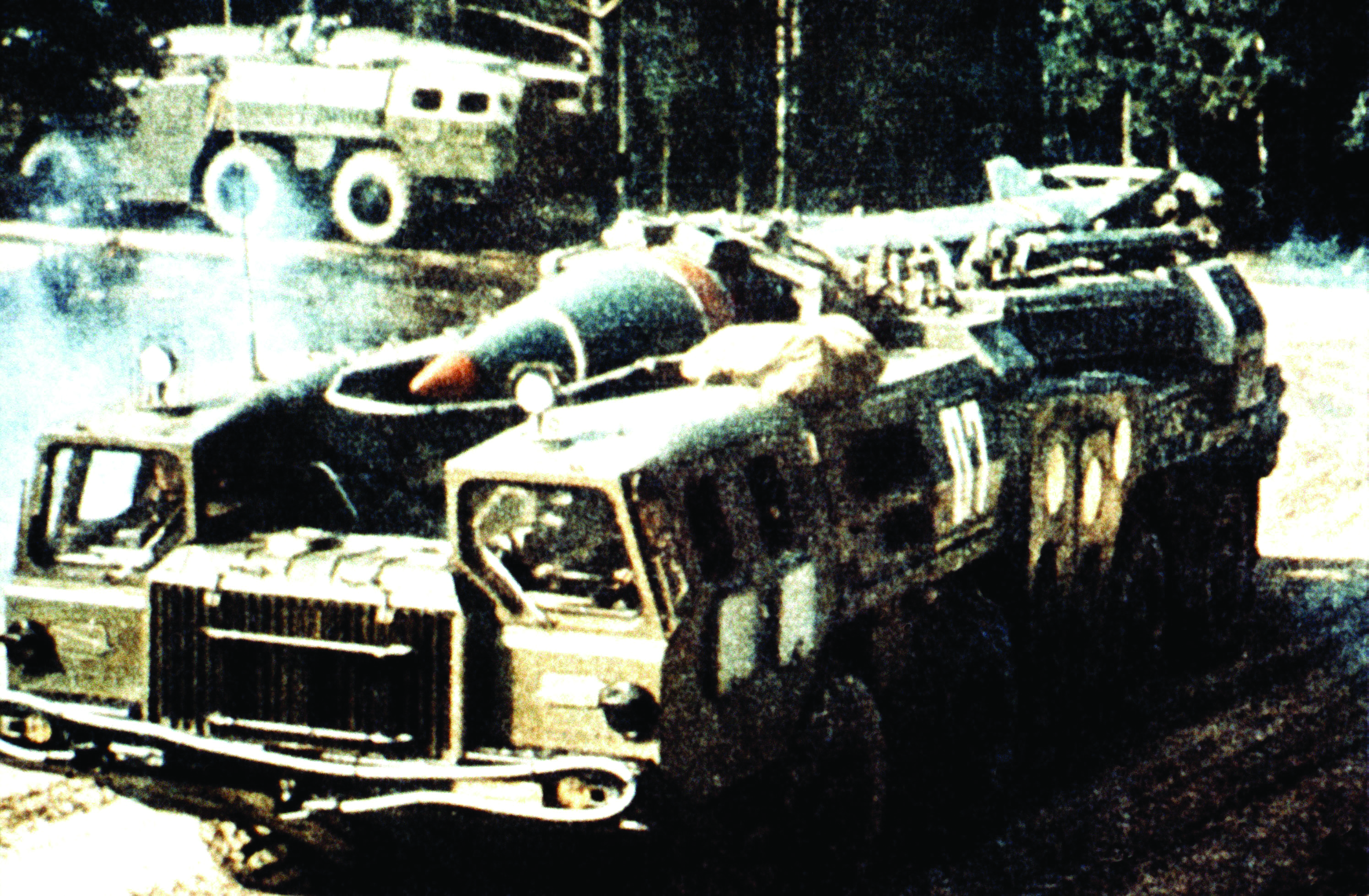 A Scud missile on its transport erector launcher (TEL), a large, camouflaged military truck, preparing for movement or launch in a field.